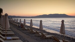 A beach with rows of sun loungers and umbrellas, a pebble beach, and a calm sea with mountains in the background. - Alexandros villa with private pool (Νωπήγεια)
