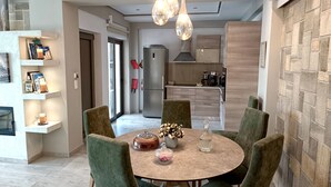A modern dining area with a round table, green upholstered chairs, and pendant lighting. - Alexandros villa with private pool (Νωπήγεια)