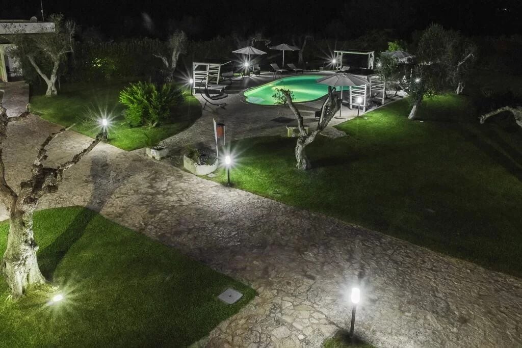 A nighttime view of a backyard with a swimming pool, stone pathway, and outdoor furniture.