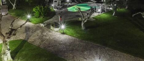 A nighttime view of a backyard with a swimming pool, stone pathway, and outdoor furniture.