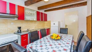 A kitchen with red cabinets, a dining table with a fruit bowl, and a white refrigerator. - Apartment Monkovic (Dubrovnik)