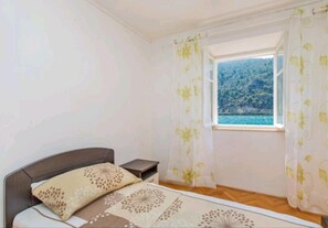 A bedroom with a bed, a nightstand, and a window with curtains. - Apartment Monkovic (Dubrovnik)