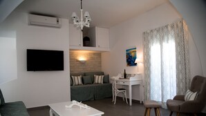 A modern living room with a flat-screen TV, a white table, a green sofa, a white desk, and a chair. - Villa Renieris in Imerovigli, Santorini (Σαντορίνη)