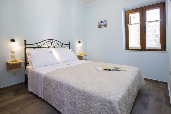 A neatly made bed with a patterned bedspread, two bedside lamps, and a window with curtains. - Traditional 2 floor villa in the heart of Lefkada (Εγκλουβή)