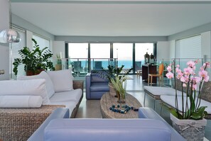 Relax in a comfortable living area with a sofa, chairs, and coffee table, offering a balcony with a view of the ocean.