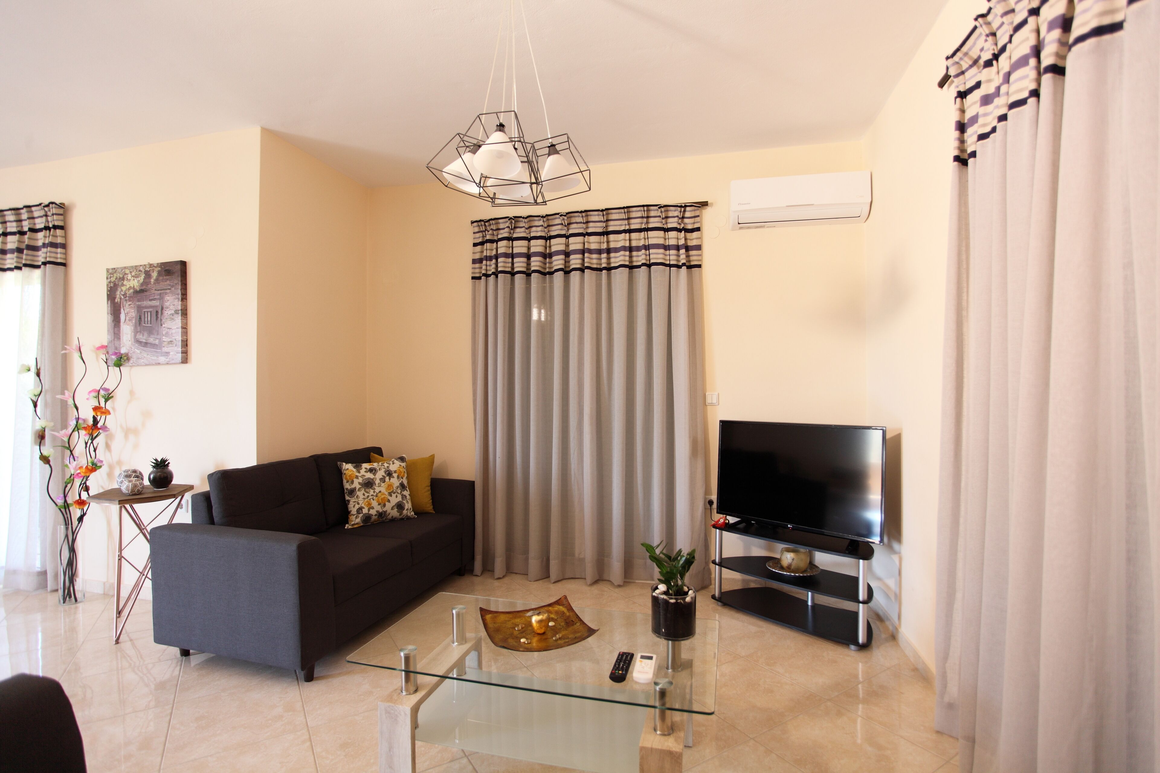 A modern living room with a sofa, a glass coffee table, a TV on a stand, and curtains.