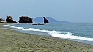 Una playa con formaciones rocosas y una montaña a lo lejos.