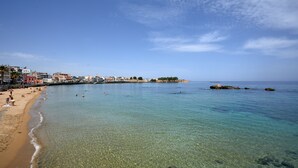 Ein Strand mit klarem Wasser, sandigem Ufer und Gebäuden entlang der Küste.