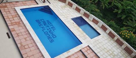 A rectangular swimming pool with a tiled border and a sign that reads "HOTEL INHABITS ARES FLUTES."