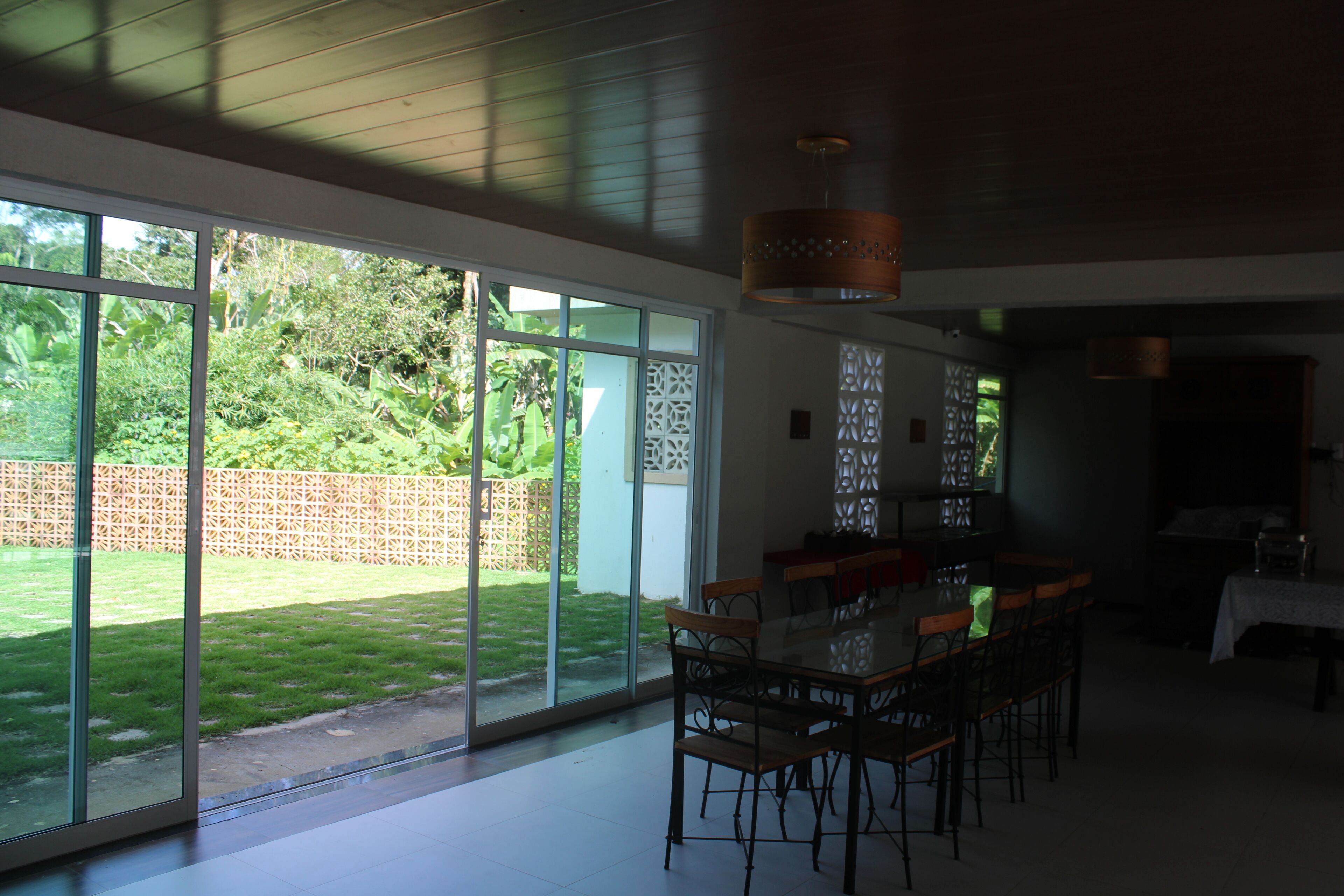Un comedor espacioso con una mesa grande y sillas, ventanas amplias que ofrecen vistas a un jardín bien cuidado y un diseño de techo moderno.