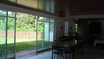 Un comedor espacioso con una mesa grande y sillas, ventanas amplias que ofrecen vistas a un jardín bien cuidado y un diseño de techo moderno.
