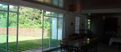 Un comedor espacioso con una mesa grande y sillas, ventanas amplias que ofrecen vistas a un jardín bien cuidado y un diseño de techo moderno.
