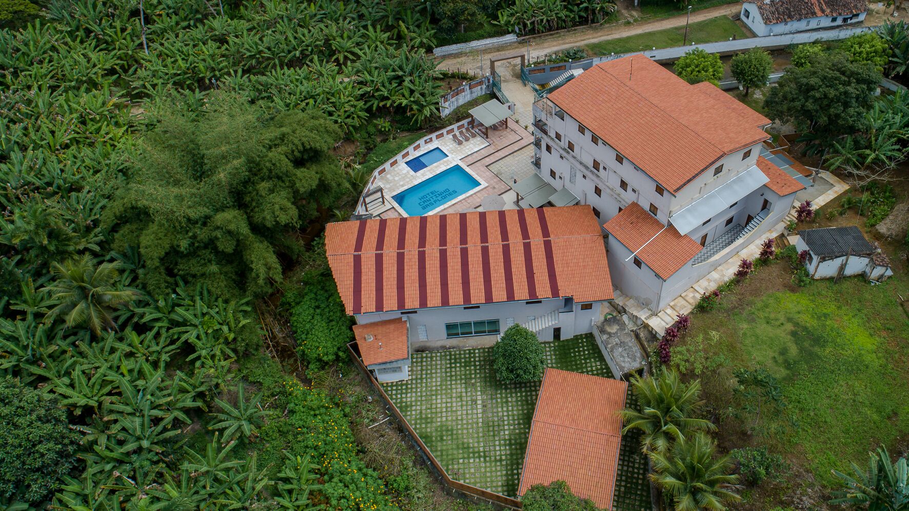 An aerial view of a hotel with multiple buildings, a swimming pool, and lush surrounding vegetation.