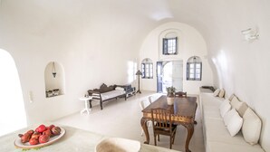 A spacious living area with a dining table, sofa, and a bowl of fruit on a counter.