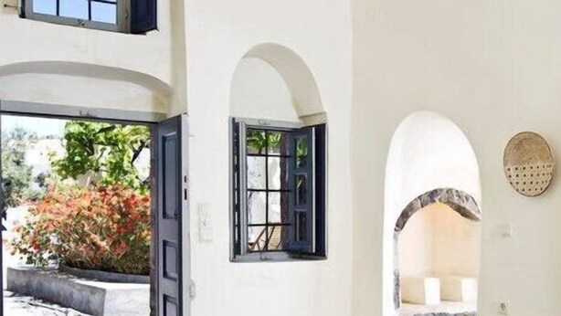 A room with a white wall, a door leading outside, and an arched doorway.