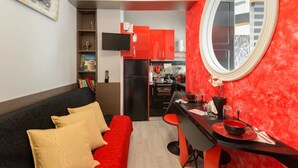 A compact living space with a red accent wall, a black sofa with yellow cushions, a dining table with red chairs, and a kitchen area with red cabinets and a black refrigerator. - ★CENTRAL LUXURY MINI SUITE JULIET★JUST RENOVATED (Θεσσαλονίκη)
