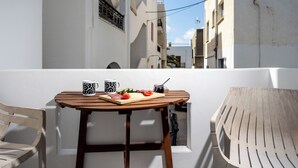 Een balkon met een houten tafel, daarop eten, een stoel en een witte muur.