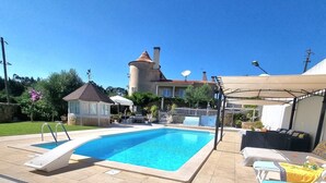 Una piscina con trampolín, sillas de descanso y un área de terraza cubierta.