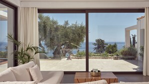 Un soggiorno moderno con un'ampia porta-finestra scorrevole che si apre su un balcone con vista sul mare e sugli alberi.