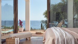 Una camera da letto con un'ampia finestra vista mare, un letto, una panca e una pianta in vaso.