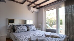 Ein Schlafzimmer mit Bett, Nachttisch, Lampe, Fernseher und einem Fenster mit Blick ins Freie.