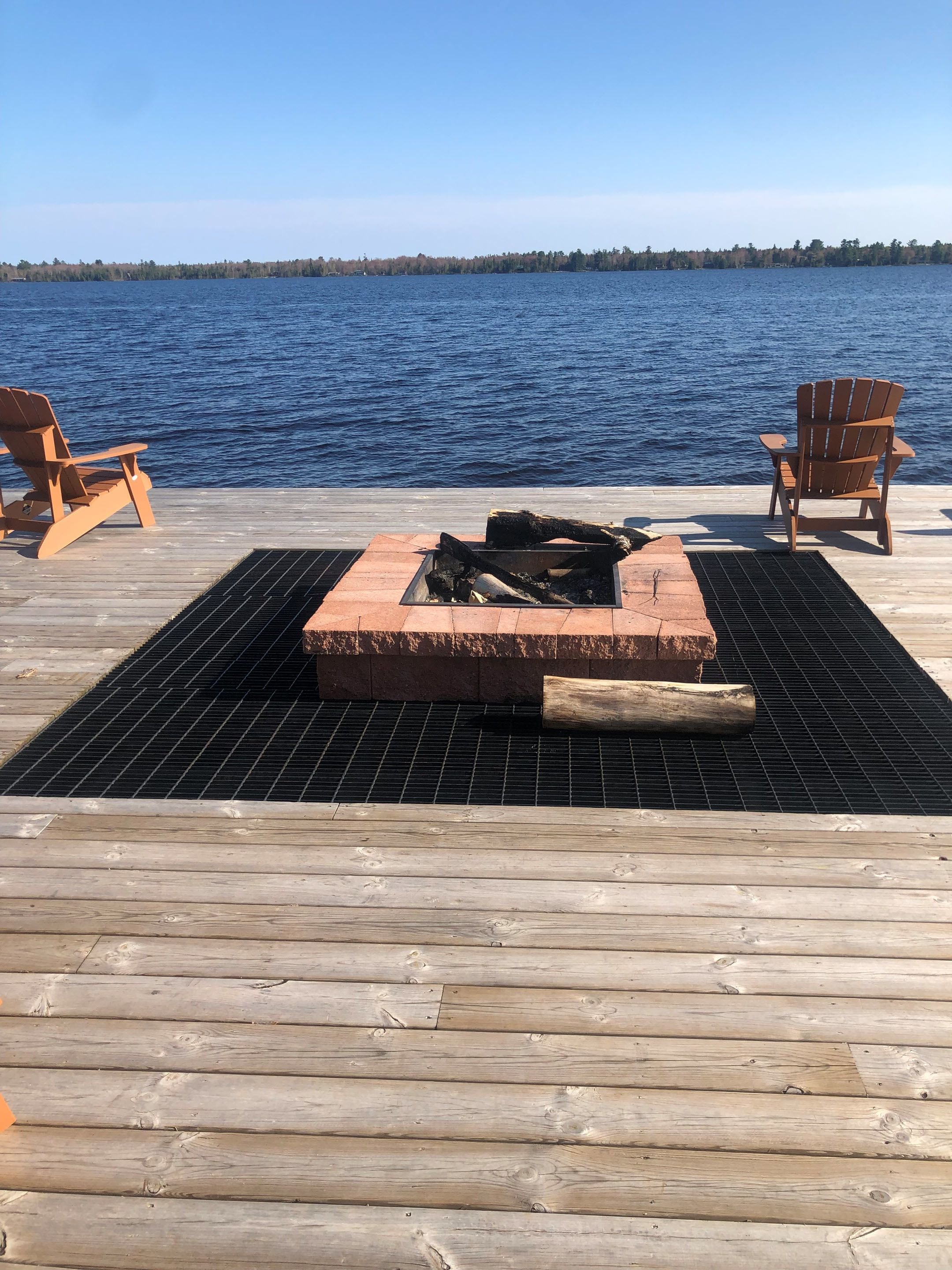 A wooden deck with a fire pit in the center, surrounded by two wooden chairs.