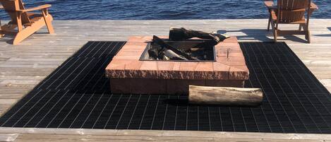 A wooden deck with a fire pit in the center, surrounded by two wooden chairs.