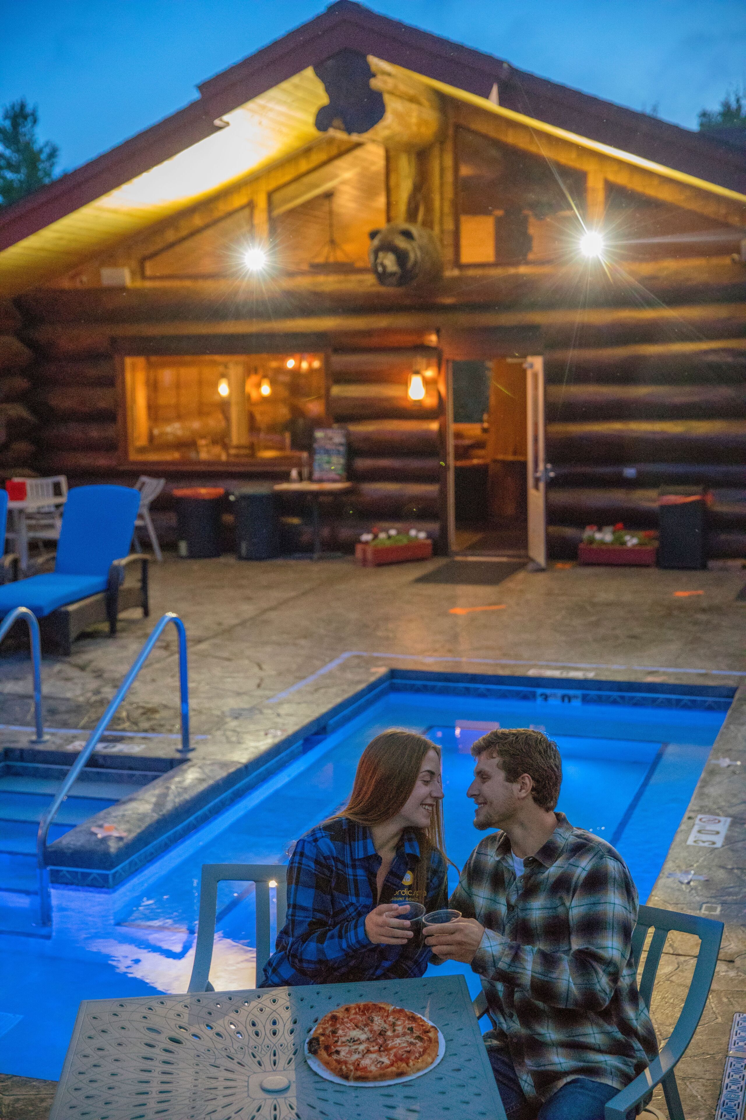 Une cabane en bois avec une piscine, un espace salon extérieur et une pizza sur la table.
