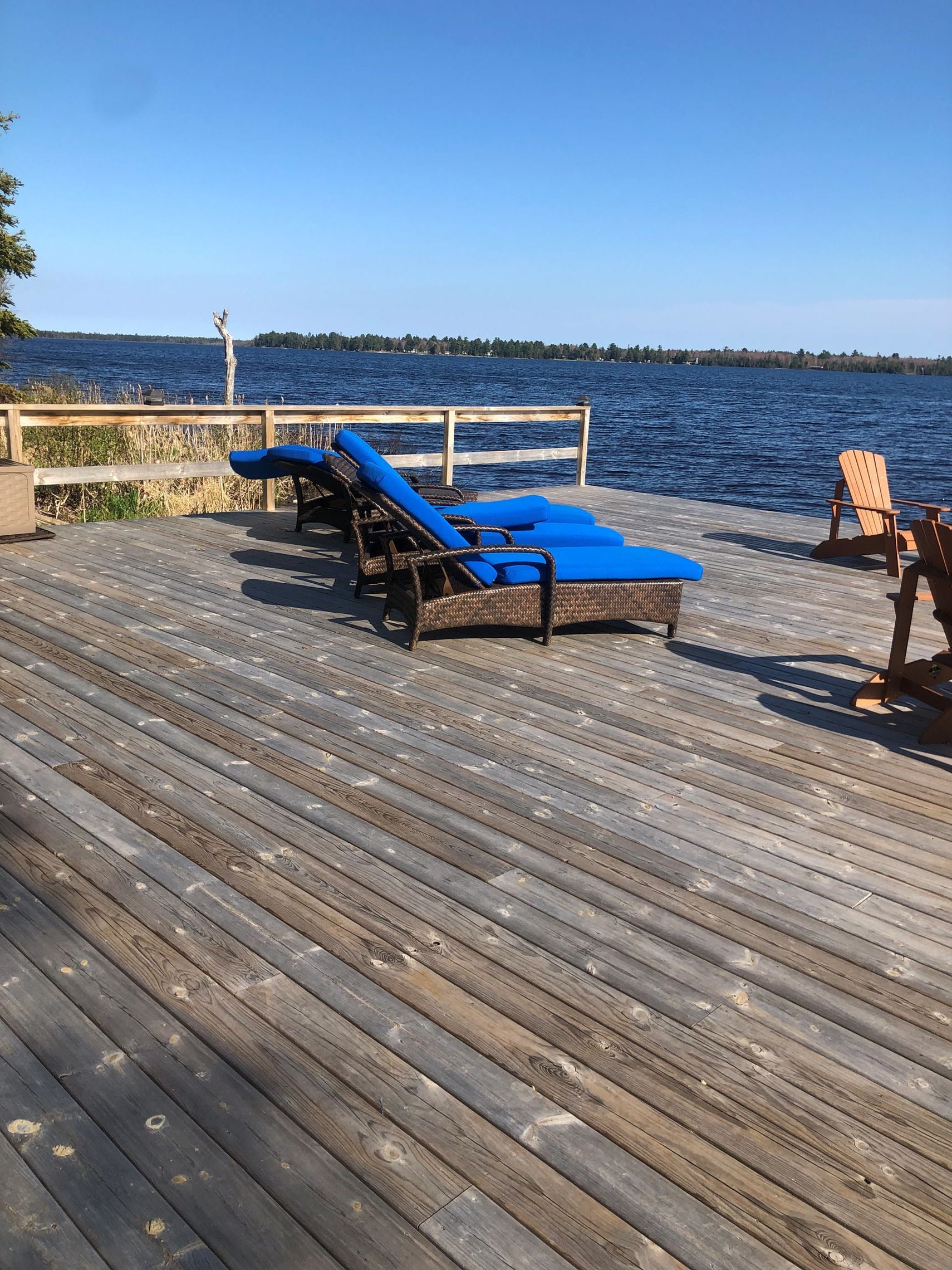 Terraza de madera con sillones de descanso y barandilla de madera, con vista a un cuerpo de agua.