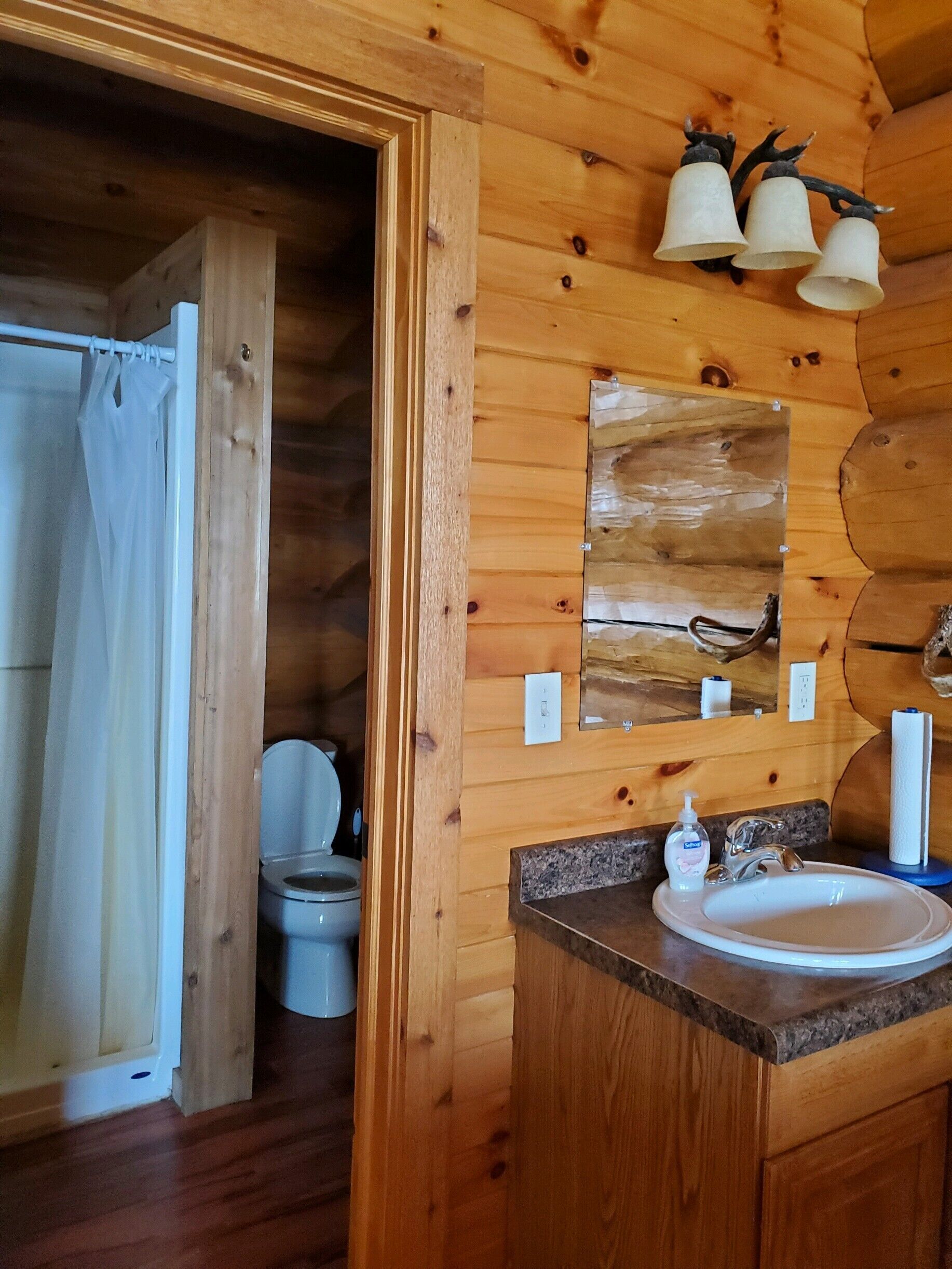 A wooden cabin bathroom with a toilet, sink, and shower curtain.