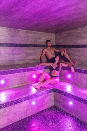 A couple relaxing in a stone-walled jacuzzi with purple lighting. - Aqua Log Cabins Resort (Mohawk)