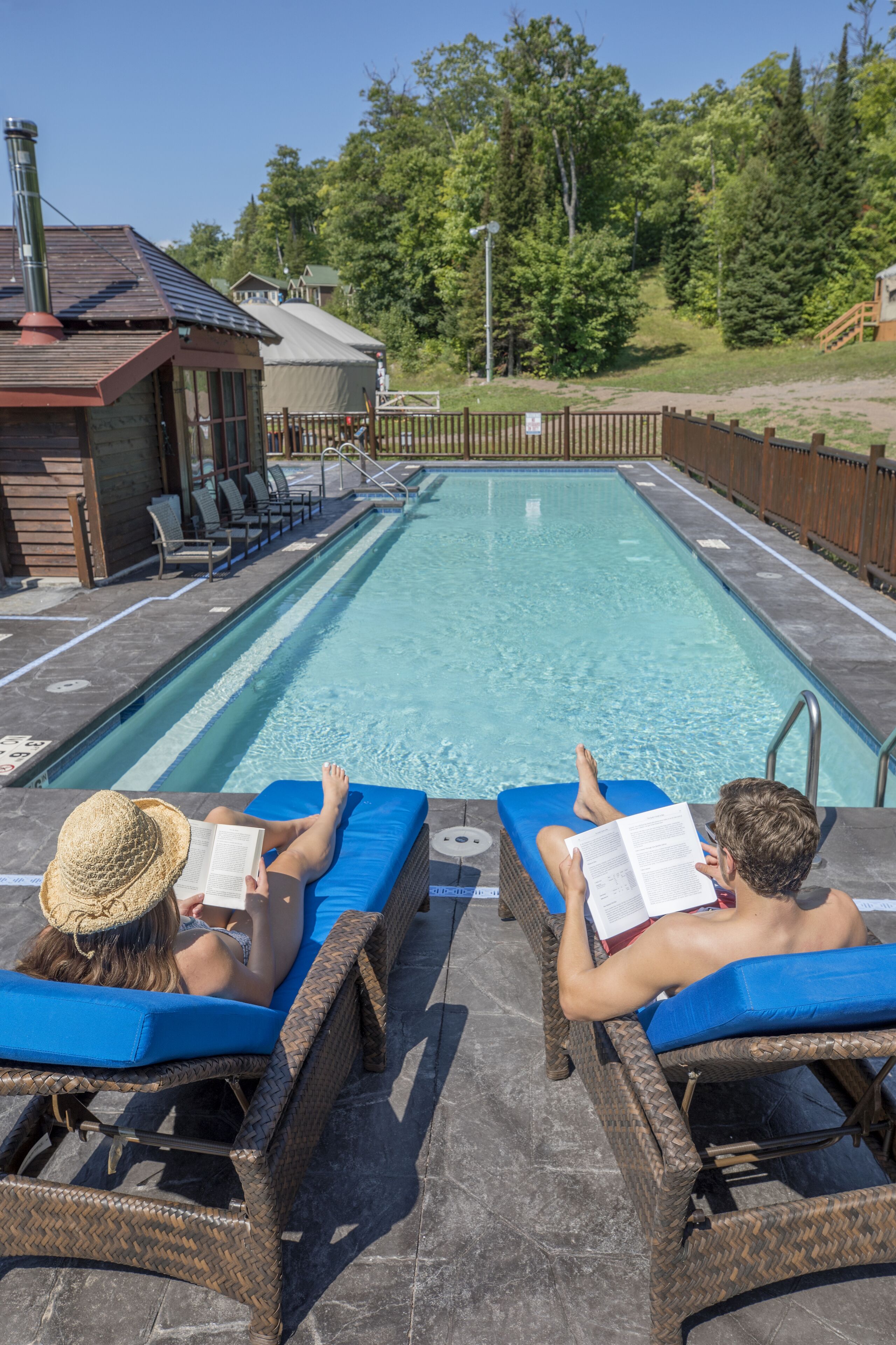 Dos sillones de relax junto a una piscina con un muelle de madera y un edificio pequeño al fondo.