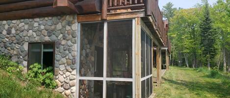 Una cabaña de madera con fachada de piedra, un balcón y un amplio ventanal que da a un espacio interior.