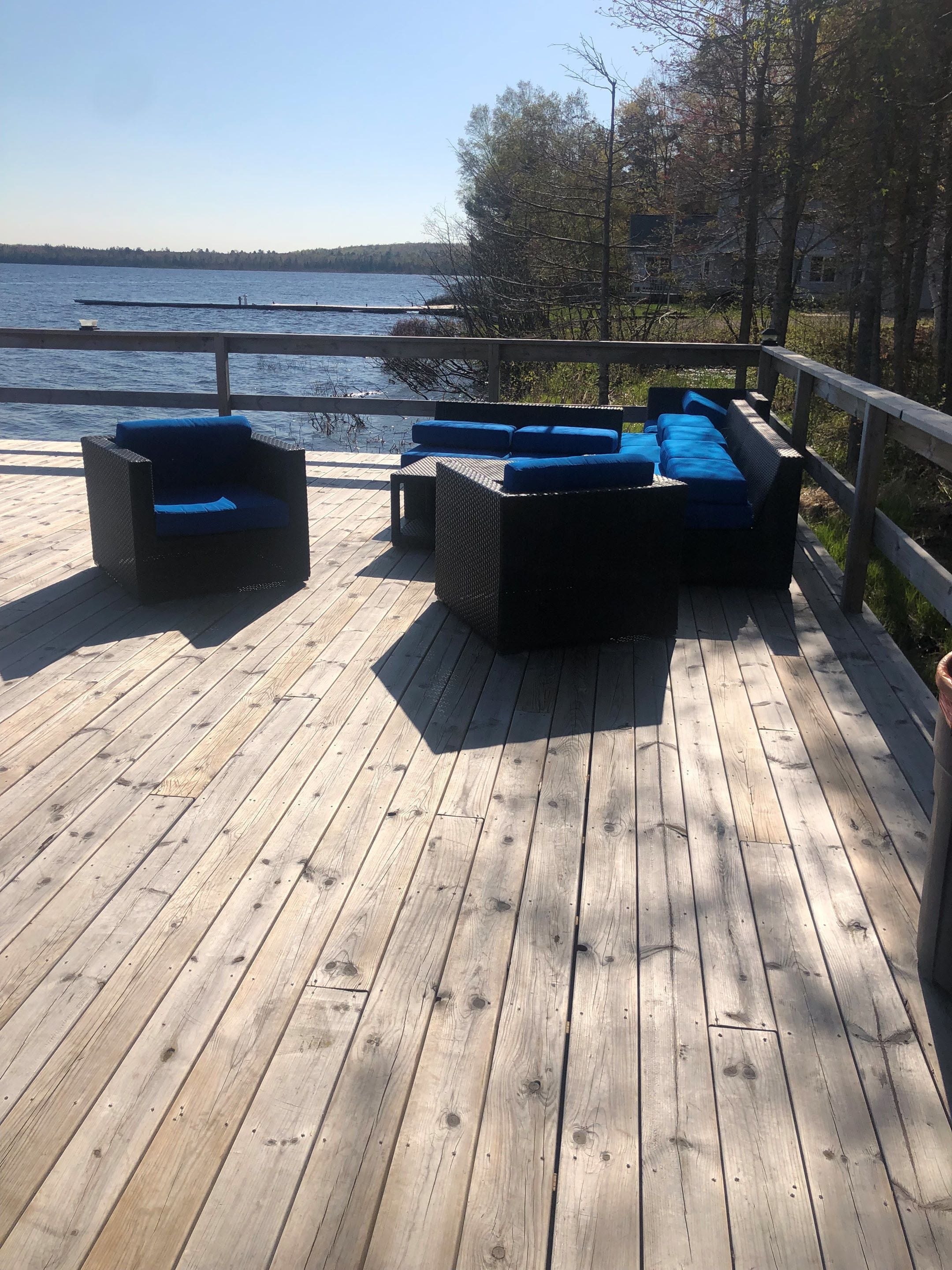 A wooden deck with outdoor furniture including a sofa and chairs, overlooking a body of water.