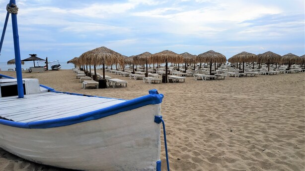 Een strand met rijen witte ligbedden en rieten parasols.