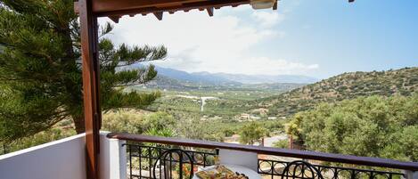 A balcony with a table and chairs, overlooking a scenic landscape with mountains and greenery.
