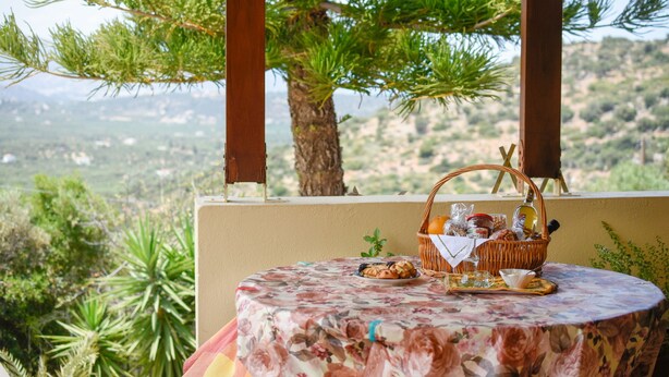 A round table with a floral tablecloth, a basket with food items, and a view of a mountainous landscape. - Villa Karmilos - A family Villa near the cretan sea and the mountains (Sissi)