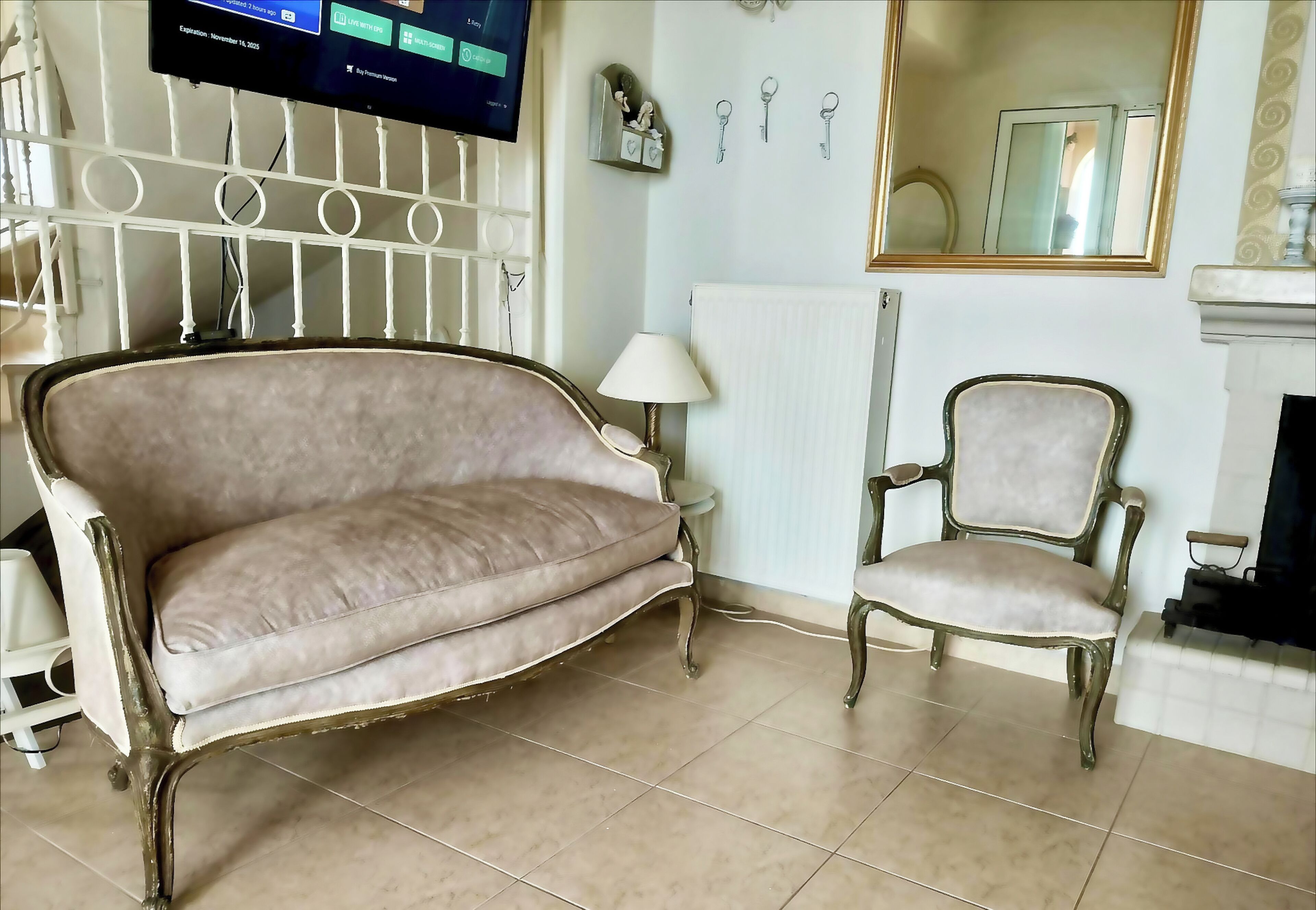 Ein Wohnzimmer mit beiger Couch, einem passenden Sessel, einem weißen Heizkörper, einem Wand-Fernseher und einem Kamin.