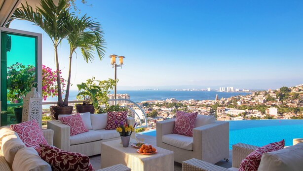 Une terrasse meublée de mobilier en osier, une vue sur la mer et un paysage urbain en arrière-plan.