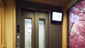 Ein Aufzug mit digitaler Anzeige, einem Wand-Fernseher und einer Kirschblüten-Wandmalerei.
