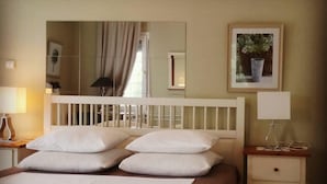 A neatly made bed with white linens and pillows, a bedside table with a lamp, and a framed picture on the wall. - Beautiful house close to Thessaloniki (Κύμινα)