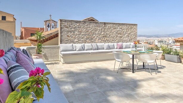A rooftop terrace with a stone wall, a cushioned seating area, and a dining table with chairs. - Pasmina Home - Stylish & cozy house, Athens, Plaka (Αθήνα)
