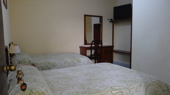 Une chambre avec deux lits, une commode, un miroir et un téléviseur posé sur une étagère.