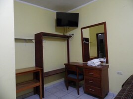 Una habitación con un escritorio de madera, una silla, un televisor en la pared y un espejo sobre el escritorio.