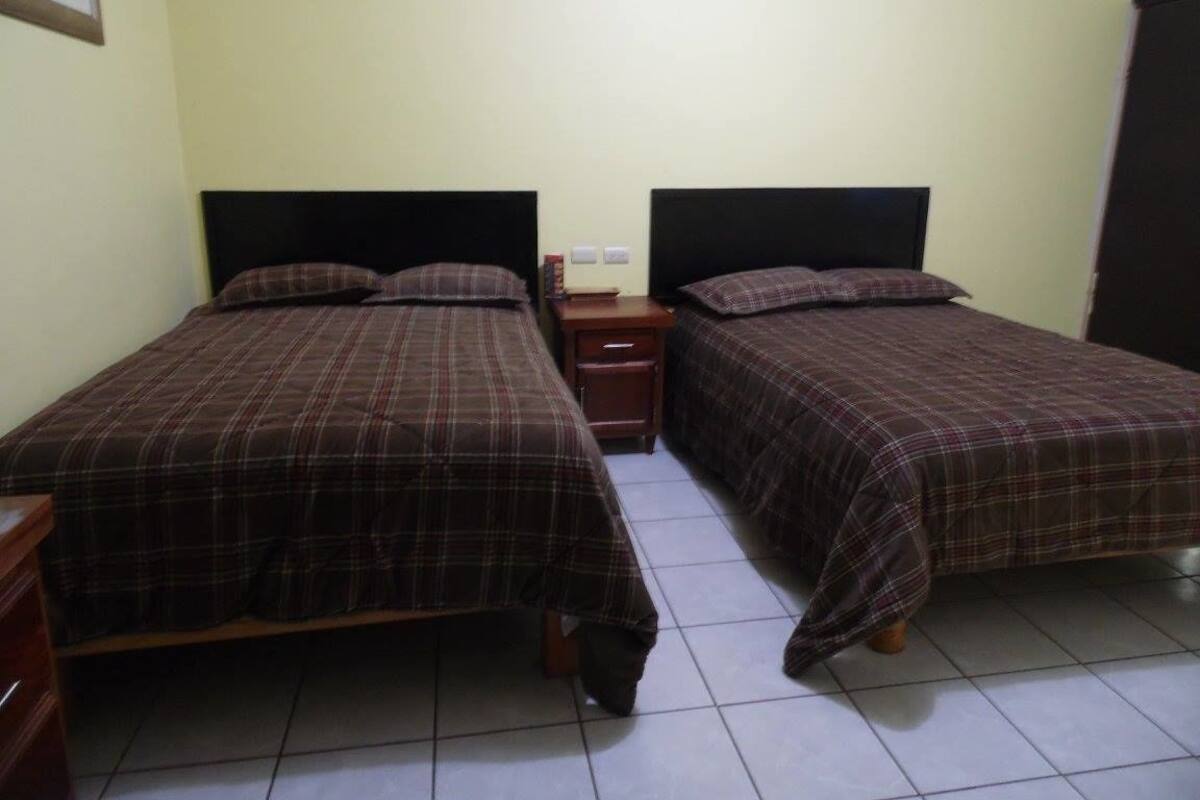 A room with two beds, each with a headboard, a nightstand, and a small table.