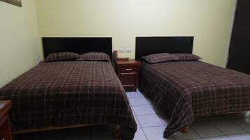 A room with two beds, each with a headboard, a nightstand, and a small table.