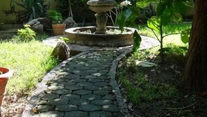A garden with a stone pathway leading to a multi-tiered fountain, surrounded by lush greenery and potted plants. - Hotel San Cristobal (Guasave)