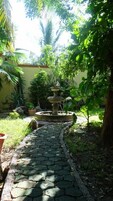 Un jardín con un sendero de piedra que conduce a una fuente escalonada, rodeado de abundante vegetación y plantas en macetas.