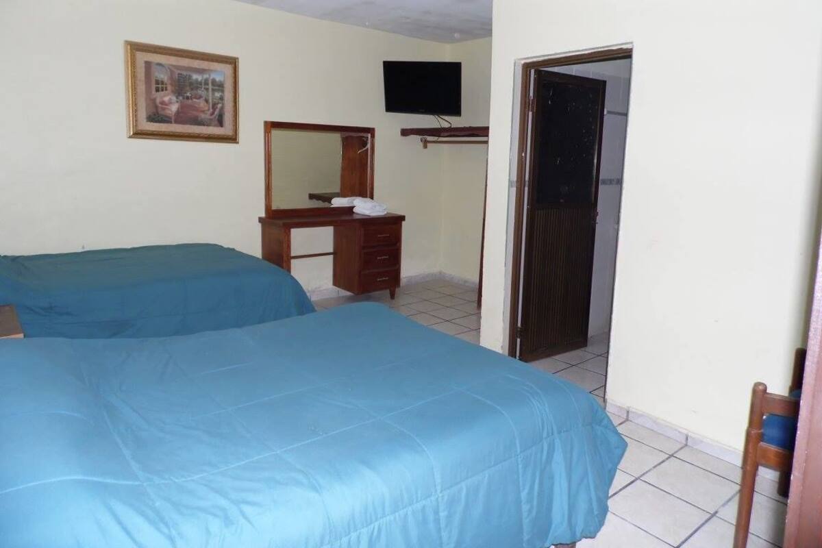 A room with two beds, a desk, a television, and a door leading to another room.