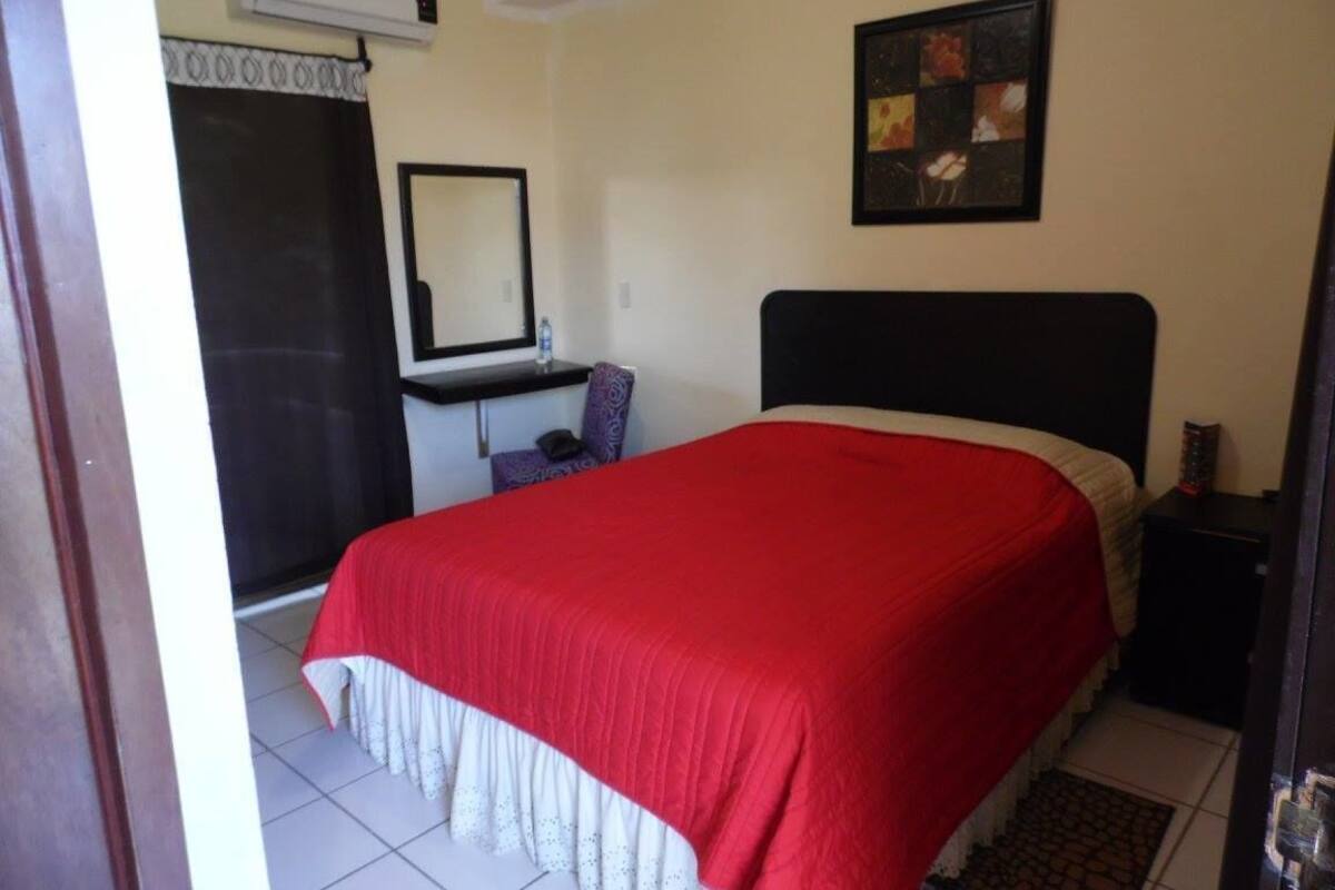 A room with a bed, a desk, a chair, a mirror, and a picture on the wall.